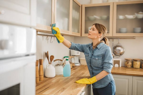 kitchencleaning Young woman using detergent or disinfectant to wash and wipe a surface at kitchen.